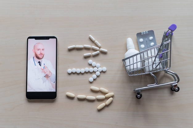 Medicina on-line Consulta remota de um médico farmacêutico em um smartphone Vista superior nas setas do smartphone dispostas em comprimidos, mini carrinho de compras e remédios sobre a mesa