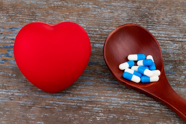 Medicina pastillas, tabletas y cápsulas en cuchara de madera con corazón