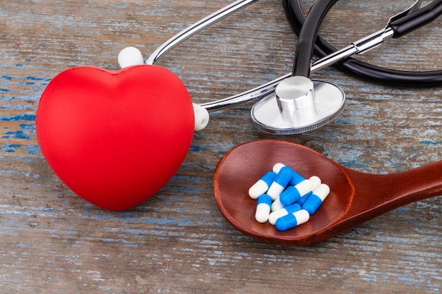 Medicina píldoras, tabletas y cápsulas en cuchara de madera con corazón.
