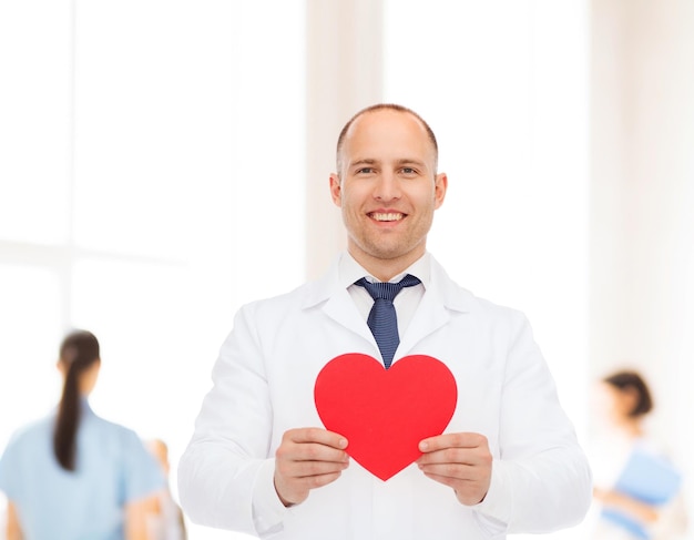 medicina, profesión, caridad y concepto de atención médica - médico sonriente con corazón rojo sobre un grupo de médicos