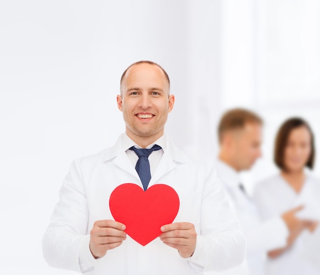 medicina, profesión, caridad y concepto de atención médica - médico sonriente con corazón rojo sobre un grupo de médicos