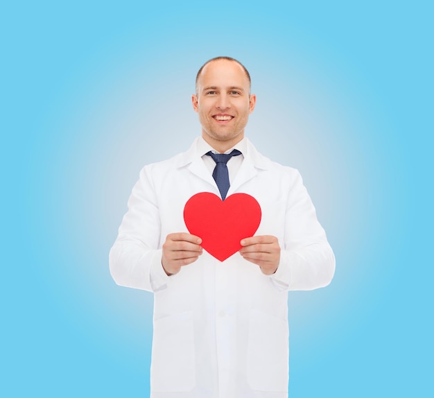 medicina, profissão, caridade e conceito de saúde - médico masculino sorridente com coração vermelho sobre fundo azul