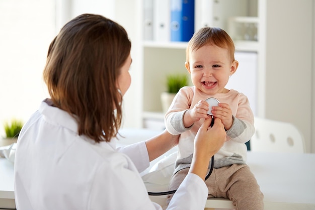 medicina, saúde, pediatria e conceito de pessoas - médico com estetoscópio ouvindo menina sorridente feliz em exame médico na clínica