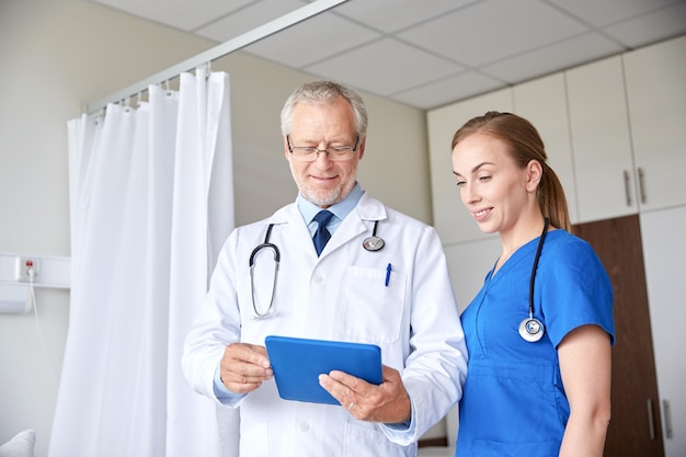 medicina, tecnología, atención de la salud y concepto de personas: médico senior y enfermera joven con computadora de tablet pc en la sala del hospital