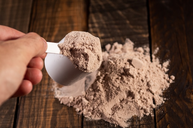 Medición de cucharada de proteína de suero en la mesa de madera para preparar un batido.