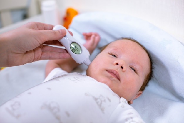 Medición de la temperatura del bebé con termómetro sin contacto. Mamá mide la temperatura corporal del bebé con un termómetro en el oído.