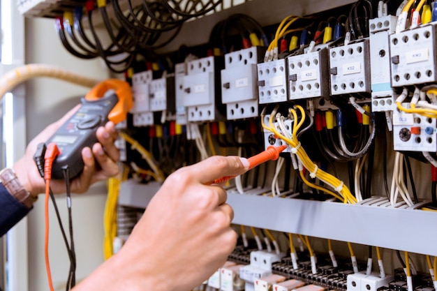 Foto mediciones de electricista con multímetro que prueba la corriente eléctrica en el panel de control.