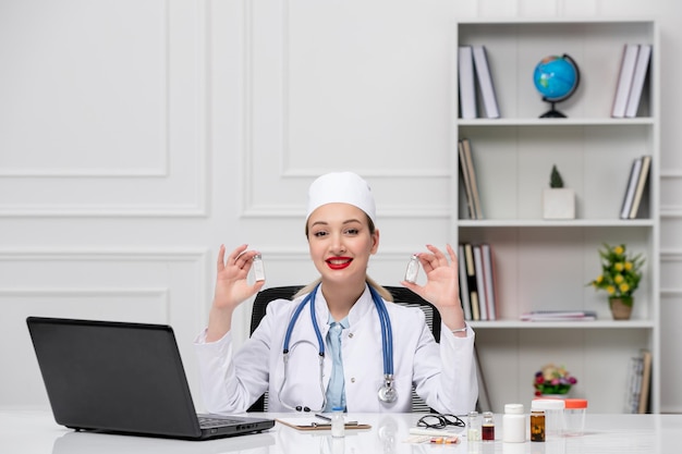Médico adorável médico de jaleco branco e chapéu com computador segurando pílulas