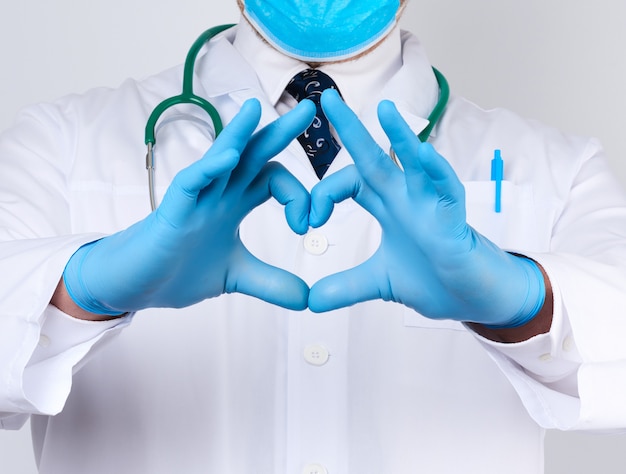 Médico adulto hombre en una bata blanca médica con un estetoscopio en el cuello muestra un gesto de corazón con las manos