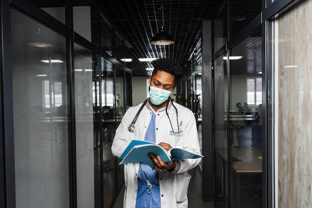 Médico africano en máscara con libros en clínica médica Estudiante de medicina negro estudia en la universidad