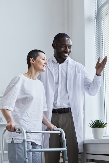 Foto médico africano de pie junto con su paciente cerca de la ventana y mirando la vista