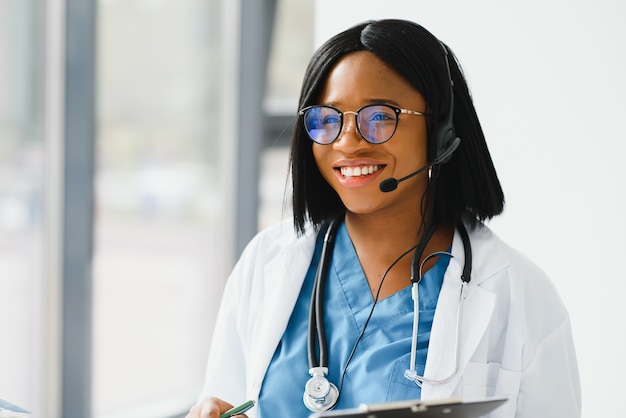 Médico africano usar fone de ouvido, consultar o paciente, fazer uma chamada de vídeo online com webcam na tela do laptop.