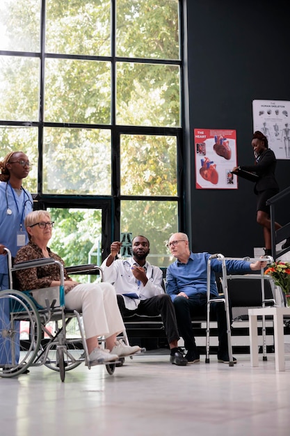 Médico afro-americano segurando radiografia de pulmões explicando perícia médica para paciente sênior com deficiência durante a consulta de check-up na área de espera do hospital. Serviço e conceito da medicina