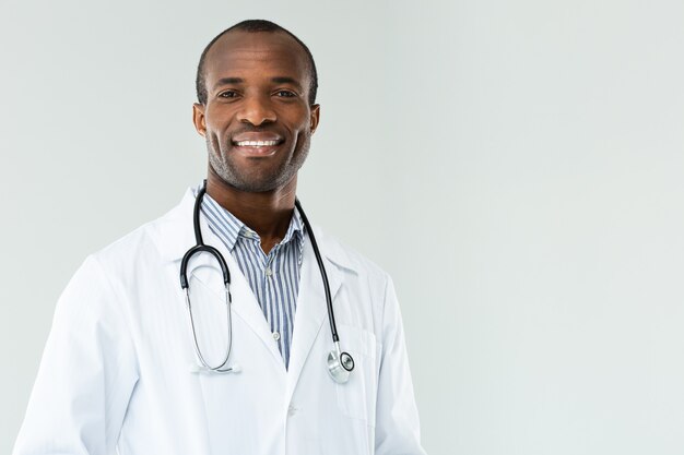 Médico afro-americano sorridente positivo em pé contra um fundo branco