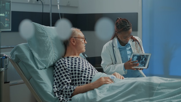 Médico afroamericano explicando la radiografía en tableta al paciente