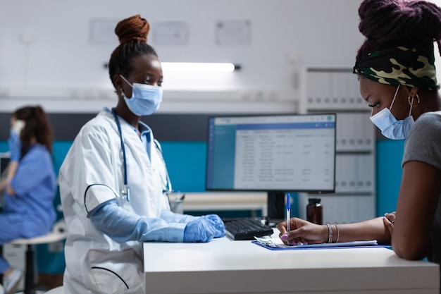 Médico afroamericano con mascarilla protectora explicando el tratamiento con medicamentos