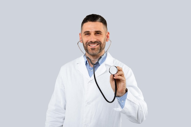 Médico amigável de meia-idade vestindo jaleco branco posando em fundo claro usando