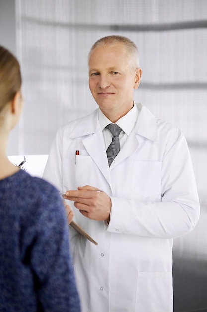 Un médico anciano y confiado consulta a una paciente en la clínica. Servicio médico perfecto en el hospital. Concepto de medicina y atención sanitaria.