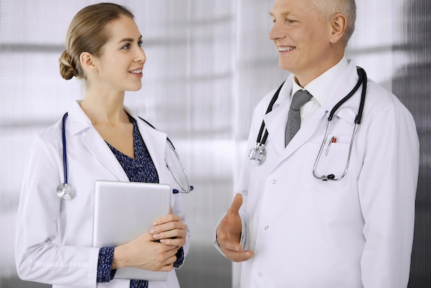 Médico anciano confiado y médico mujer discutiendo la terapia actual de la enfermedad mientras está de pie en la clínica. Trabajo en equipo en el hospital. Concepto de medicina y salud.