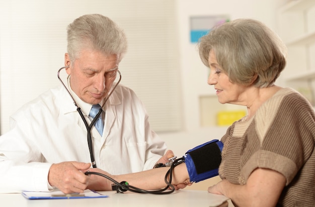 Médico anciano midiendo la presión arterial de la mujer mayor