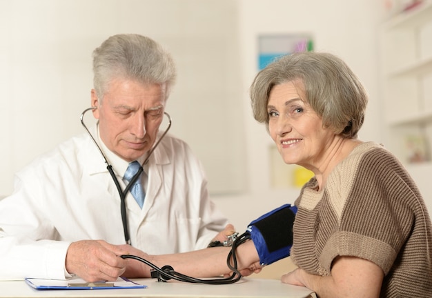 Médico anciano midiendo la presión arterial de la mujer mayor