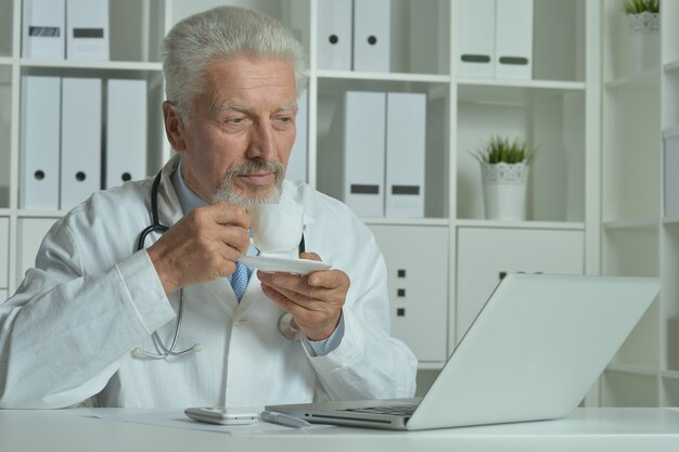 Médico anciano con un portátil en la oficina