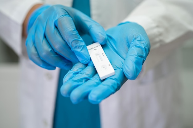 Foto médico asiático em fato de ppe mostra resultado positivo do teste com kit de teste de antígeno de saliva