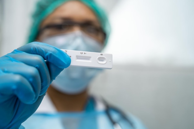 Médico asiático em traje de EPI segurando o kit de teste de antígeno de saliva para verificar o coronavírus Covid19 no hospital