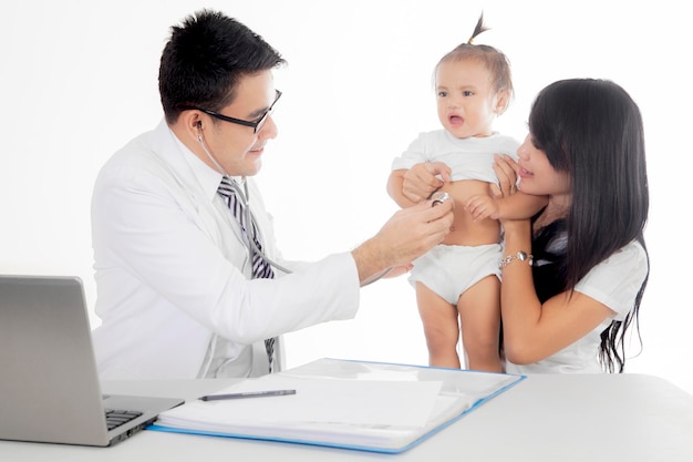 Médico asiático examinando uma menina com um estetoscópio isolado sobre um fundo branco