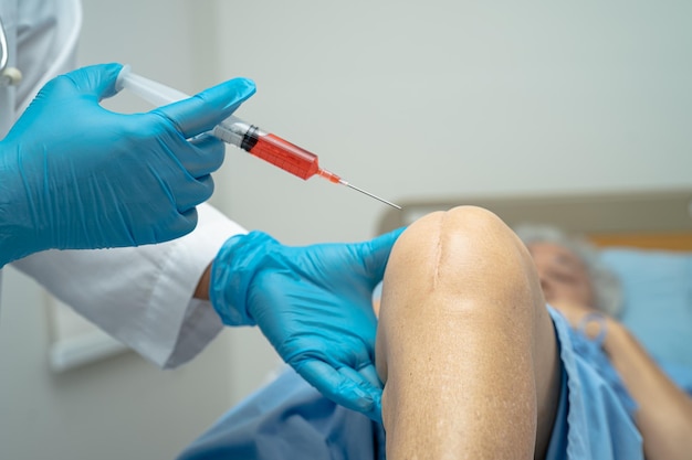 Médico asiático injeta plasma rico em plaquetas de ácido hialurônico no joelho de uma mulher idosa para andar sem dor