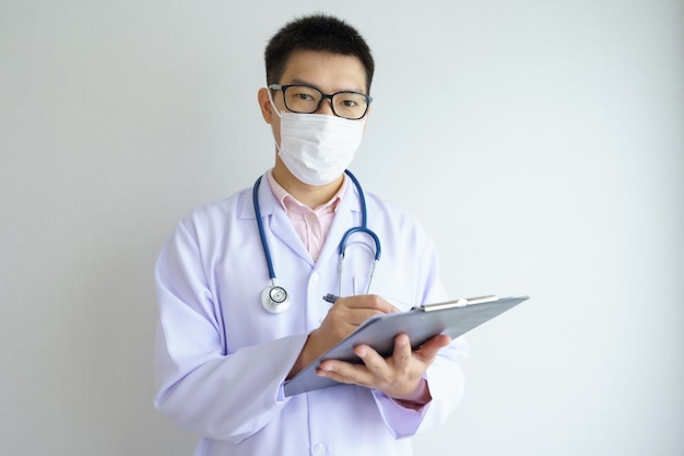 Médico asiático masculino que trabaja en la oficina del hospital con mascarilla para proteger los virus Covid 19.