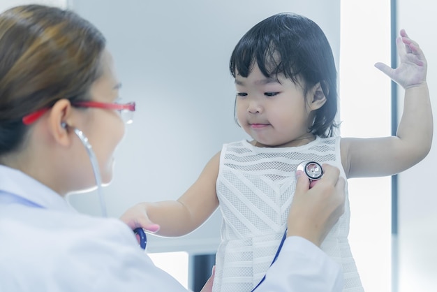 Un médico asiático que usa un estetoscopio para comprobar su respiración y el corazón de una chica encantadora comprueba la salud de los niños de Tailandia