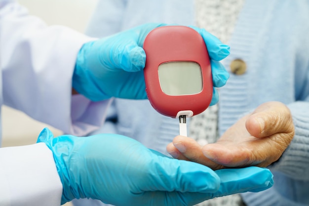 Médico asiático que utiliza un medidor de glucosa digital para comprobar el nivel de azúcar en la sangre de la muestra para el tratamiento de la diabetes
