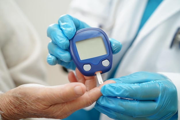 Médico asiático que utiliza un medidor de glucosa digital para comprobar el nivel de azúcar en la sangre de la muestra para el tratamiento de la diabetes