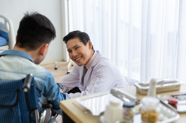 Médico asiático revisando, consultando y alentando a un paciente joven discapacitado