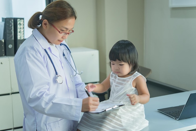 El médico asiático tiene un estetoscopio para controlar su respiración y el corazón de una niña encantadora para controlar la salud de los niños de Tailandia