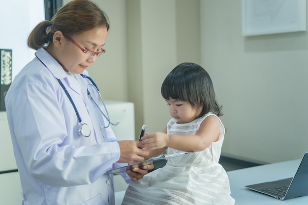 El médico asiático tiene un estetoscopio para controlar su respiración y el corazón de una niña encantadora para controlar la salud de los niños de Tailandia