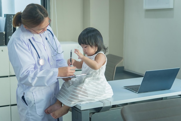 El médico asiático tiene un estetoscopio para controlar su respiración y el corazón de una niña encantadora para controlar la salud de los niños de Tailandia