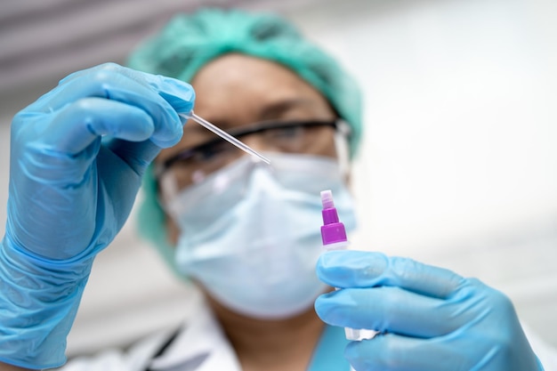 Médico asiático con traje de PPE que sostiene el kit de prueba de antígeno de saliva para verificar el coronavirus Covid19 en el hospital