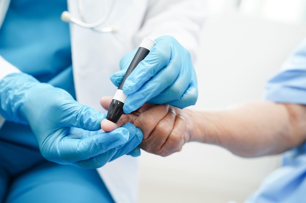 Médico asiático usando caneta lancet no dedo do paciente sênior para verificar o nível de açúcar no sangue da amostra