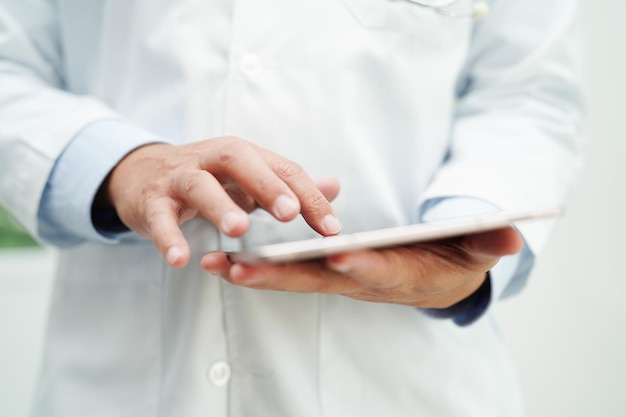 Médico asiático usando computador tablet para ler o relatório do paciente, verificar e procurar resolver
