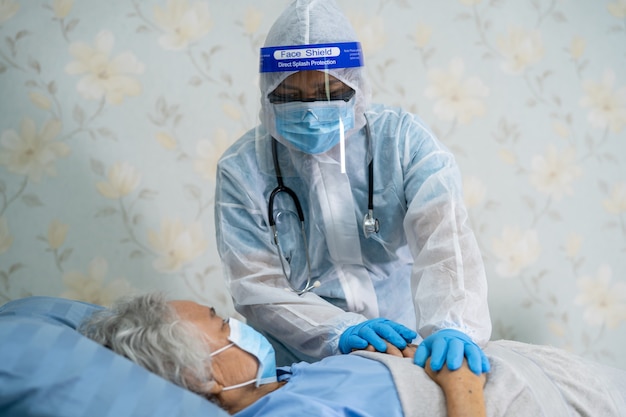 Médico asiático usando protetor facial e traje de proteção individual novo normal para verificar a segurança da infecção do paciente contra surto de coronavírus covid-19 na enfermaria de quarentena do hospital.