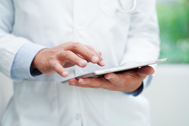 Médico asiático usando tablet para ler o relatório do paciente e procurar uma solução