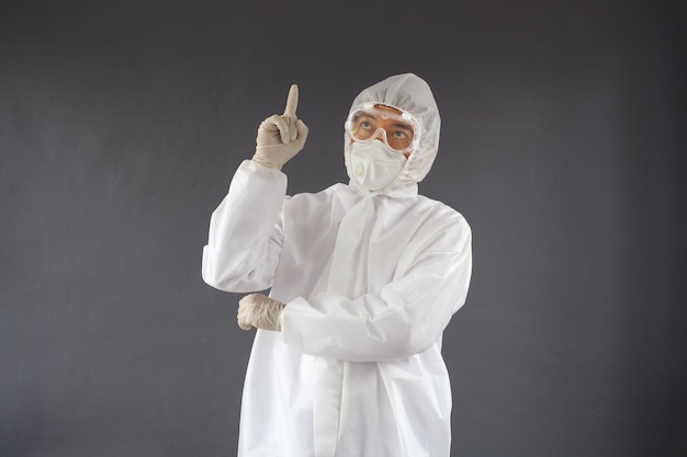 Médico asiático usando traje de proteção e óculos de segurança com o dedo indicador apontando para cima tendo uma ideia