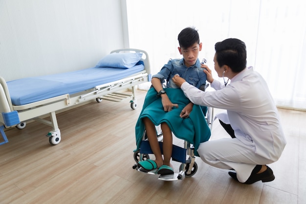 Médico asiático utiliza un estetoscopio para comprobar la discapacidad del paciente en silla de ruedas