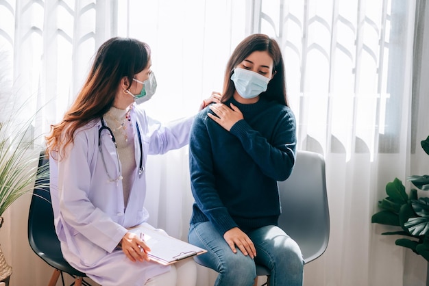 Un médico asiático visita y examina a una mujer adulta joven en el hospital con síntomas de síndrome de oficina El médico revisa y consulta por atención médica usando una máscara para proteger la pandemia de covid19