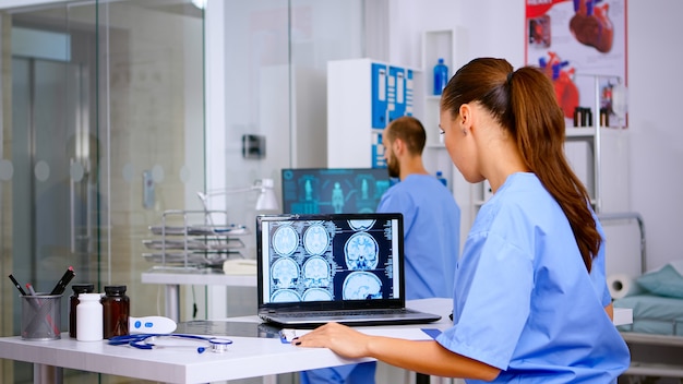 Foto médico assistente especialista em uniforme médico examinando filme de raio-x digital e escrevendo diagnóstico na área de transferência na clínica do hospital, anotando o tratamento para o paciente. radiologista analisando radiografia