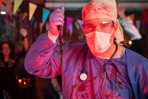 Médico assustador segurando uma faca com sangue na festa de celebração do halloween. Fantasia de Dia das Bruxas.