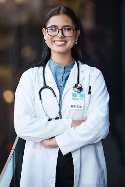 Médico de atención médica y retrato de una mujer con sonrisa y anteojos en el vestíbulo del hospital en una feliz misión para ayudar a la orgullosa líder femenina en el campo médico con confianza en la visión y liderazgo en una clínica en India