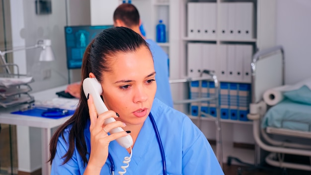 Médico atendendo telefone na recepção do hospital, telessaúde, checando lista de pacientes agendados. Médico assistente conversando ao telefone com a pessoa doente durante a consulta.